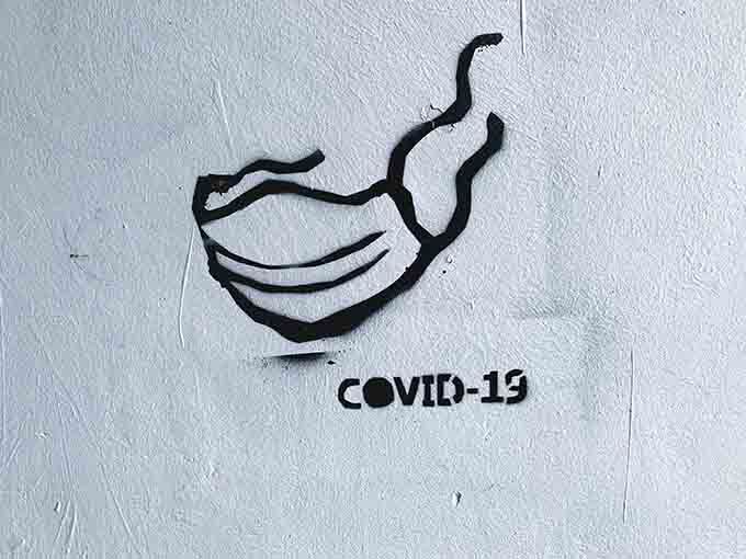 Grafiti em parede com uma máscara e o nome Covid-19.