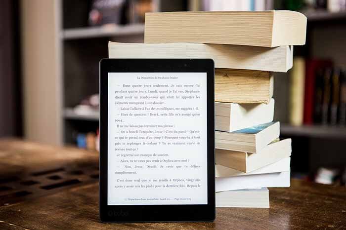 Tablet com e-book aberto e atrás alguns livros empilhados.