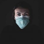 Fundo prevo e mulher em primeiro plano com máscara para se proteger da pandemia do novo coronavírus