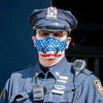Policial usa máscara de proteção com estampa da bandeira americana no bairro do Brooklyn, em Nova York.
