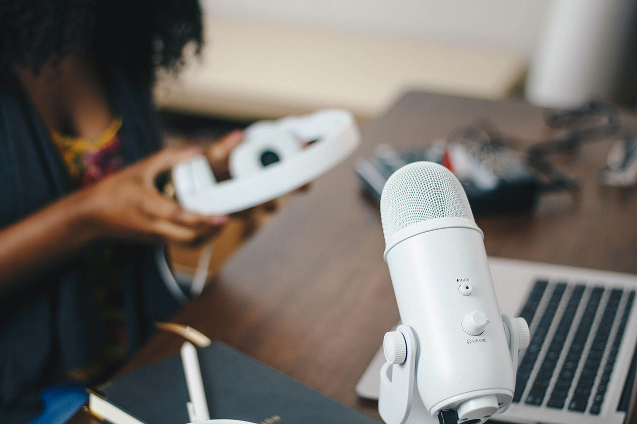 Em uma mesa aparece um microfone, tipicamente usado por podcasters. Modalidade é uma da história digital.